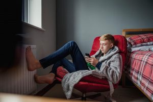 A teenage boy uses his phone and relaxes in his bedroom.