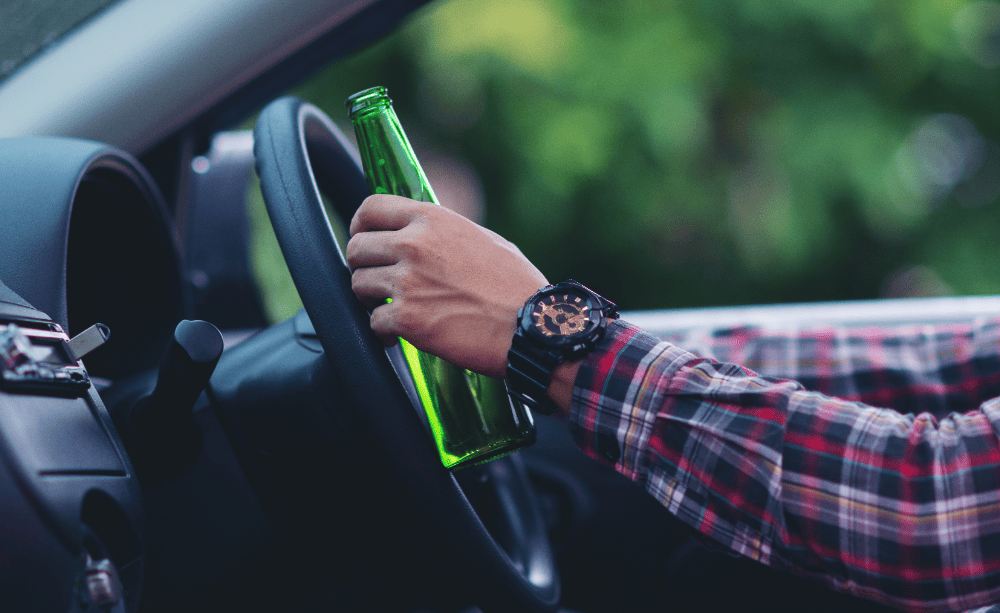 A motorist holding a beer while behind the wheel of a vehicle.